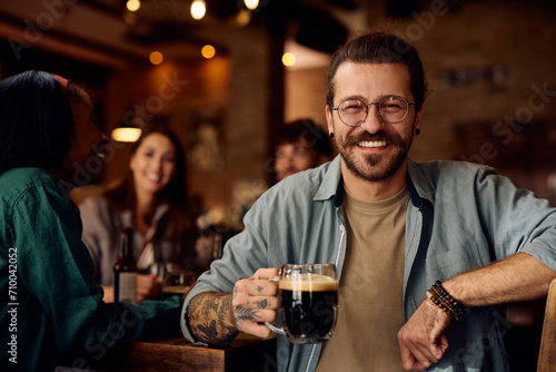 Happy man enjoying in glass of beer with his friends in bar and looking at camera.