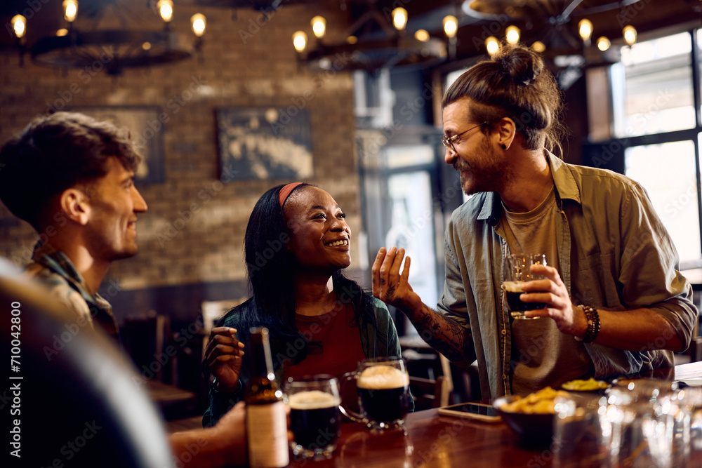 Happy black woman and her friend talking and drinking beer in pub.