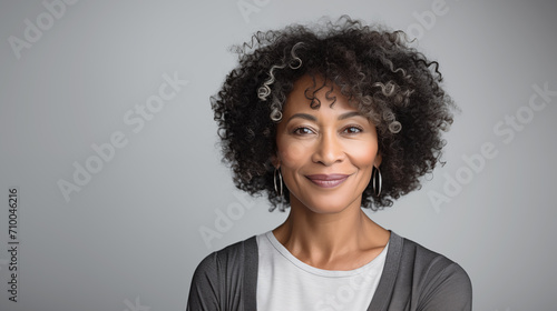 Beautiful mature black woman in her 50s with curly hair and perfect skin, looking at the camera smiling, isolated in a grey background photo