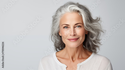 Beautiful mature woman in her 50s with gray hair and perfect skin, smiling at the camera, isolated on white background