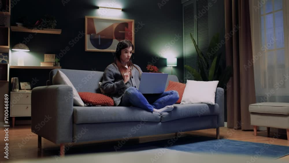Woman sitting at sofa with legs. Female wearing headphones and conducting video call. Woman holding laptop and working. Female conducting online webinar. Woman talking in microphone. Woman sitting at sofa with legs. Female wearing headphones and conducting video call. Woman holding laptop and working. Female conducting online webinar. Woman talking in microphone.