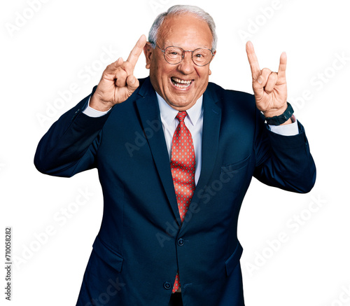 Senior man with grey hair wearing business suit and glasses shouting with crazy expression doing rock symbol with hands up. music star. heavy music concept.