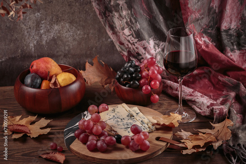 Cheese platter served with red wine, autumn fruits and dry leaves on dark wooden background. Appetizer of blue cheese on cutting board with grapes and wine