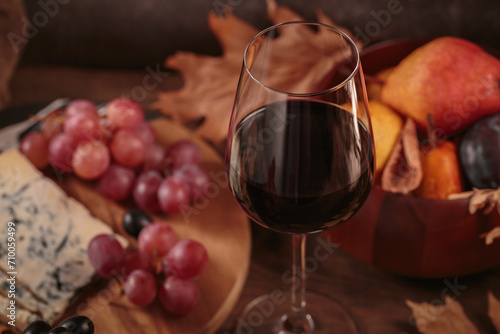 Glass of red wine served with blue cheese on dark wooden background. Autumn picnic with wine and cheese platter, fruits and dry leaves in rustic style