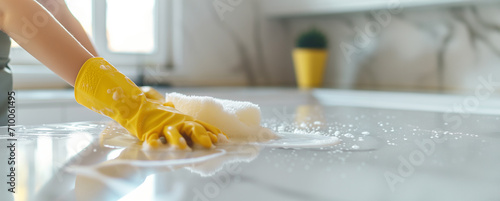 Woman in yellow gloves cleaning table. In light, modern, minimalistic kitchen. Cleaning concept, banner with copy space for eco-friendly article or for cleaning service.