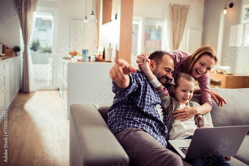 Foto Happy excited young family using laptop on sofa at home