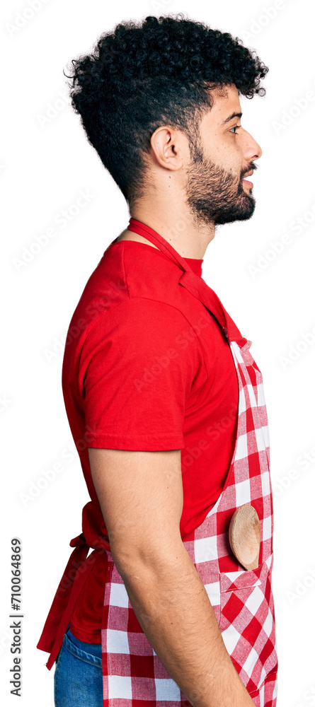 Young arab man with beard wearing cook apron looking to side, relax profile pose with natural face with confident smile.