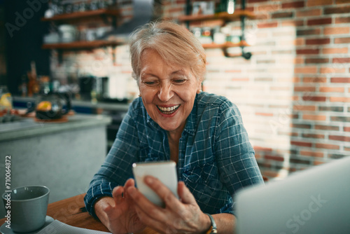 Senior woman smiling while using smartphone in kitchen photo