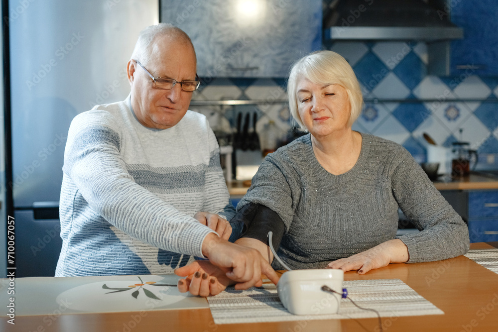 An elderly man measures his wife's blood pressure and presses the button on the tonometer. An elderly man measures his wife's blood pressure and presses the button on the tonometer.