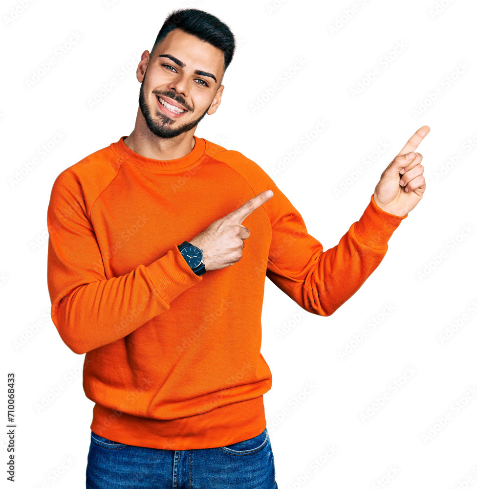 Young hispanic man with beard wearing casual orange sweater smiling and looking at the camera pointing with two hands and fingers to the side. Young hispanic man with beard wearing casual orange sweater smiling and looking at the camera pointing with two hands and fingers to the side.