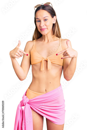 Beautiful brunette young woman wearing bikini and sunglasses looking confident with smile on face, pointing oneself with fingers proud and happy.