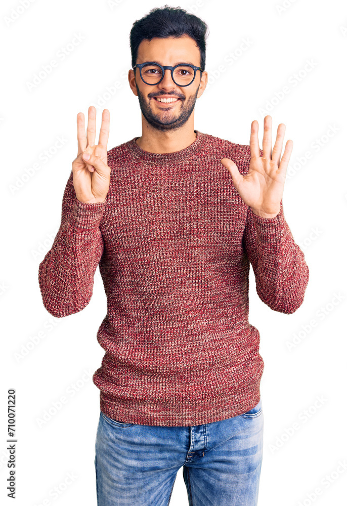 Naklejka premium Young handsome hispanic man wearing winter sweater and glasses showing and pointing up with fingers number eight while smiling confident and happy.