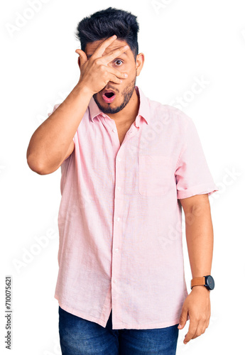 Handsome latin american young man wearing casual summer shirt peeking in shock covering face and eyes with hand, looking through fingers with embarrassed expression.