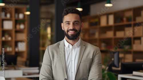 A sharply dressed professional in a smart casual olive green blazer stands with a friendly smile in a well-appointed office, embodying a blend of formality and approachability.