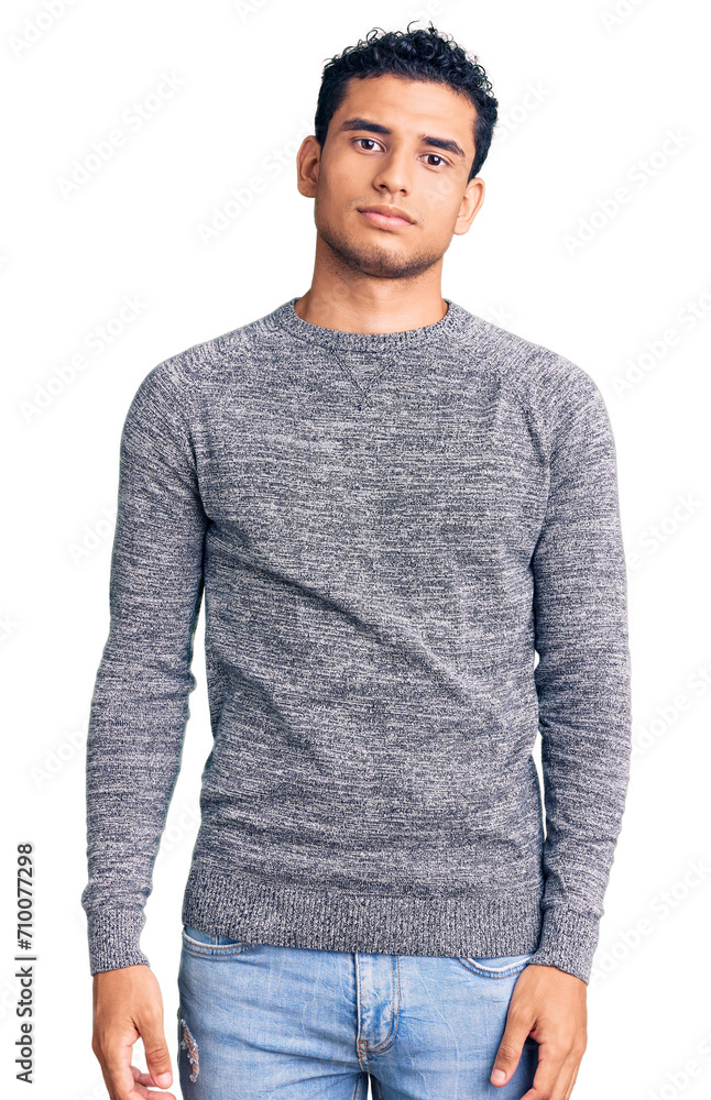 Hispanic handsome young man wearing casual sweater relaxed with serious expression on face. simple and natural looking at the camera. Hispanic handsome young man wearing casual sweater relaxed with serious expression on face. simple and natural looking at the camera.
