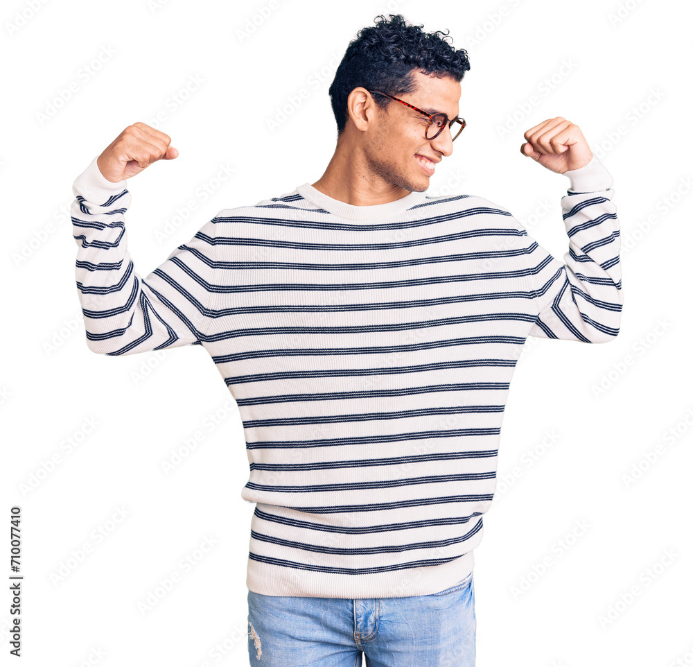 Naklejka premium Hispanic handsome young man wearing casual clothes and glasses showing arms muscles smiling proud. fitness concept.