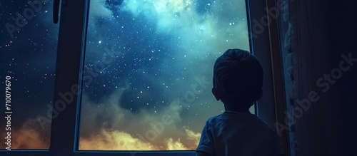Child gazes at night sky through window.