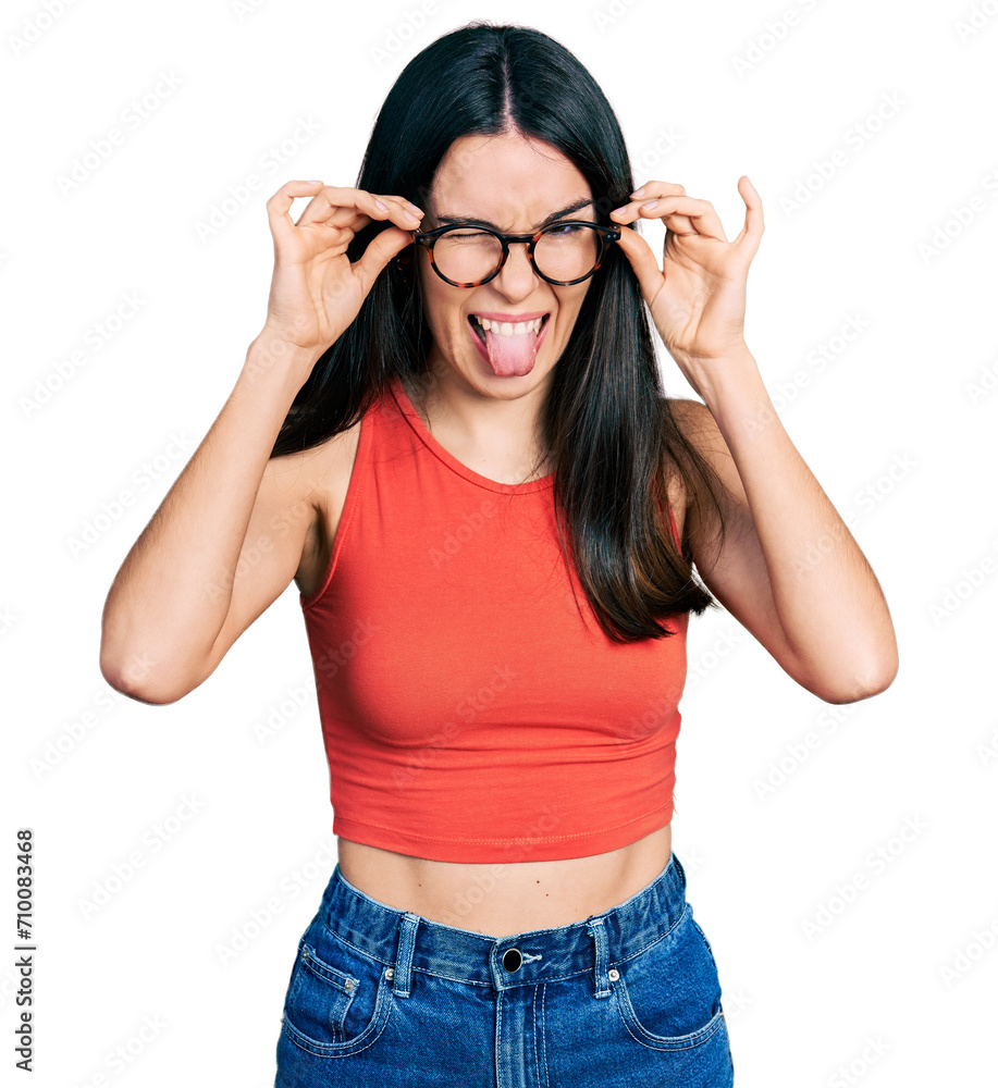 Young hispanic woman wearing casual clothes and holding glasses sticking tongue out happy with funny expression. Young hispanic woman wearing casual clothes and holding glasses sticking tongue out happy with funny expression.