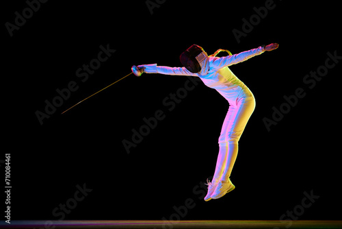 Strength and grace. Combination of strength and grace necessary in the art of fencing. Female athlete, fencer in motion over black background in neon light. Concept of sport, competition, hobby