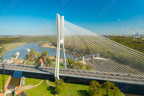 Long pylon bridge spanning Oder river against sunny Wroclaw. Cars drive on cable-stayed Redzinski Bridge among scenic city parks aerial view photo