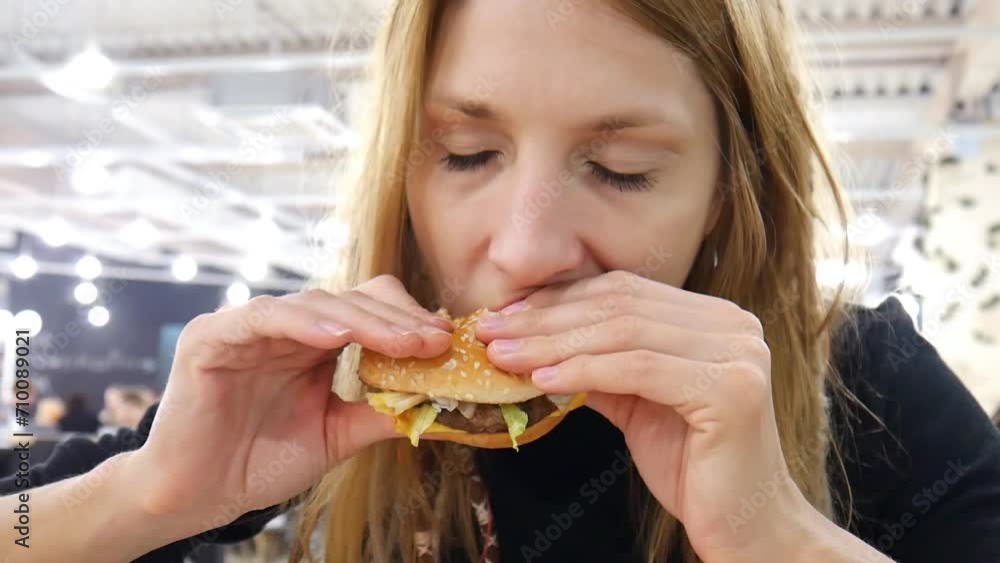 A cute lady bites a hamburger in her hands in a fast food restaurant A cute lady bites a hamburger in her hands in a fast food restaurant
