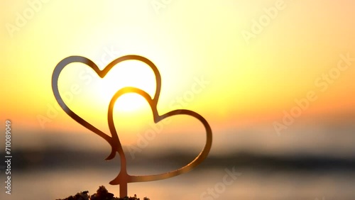 Two black outlines of heart at dawn and sunset on sky on seashore. Stick contours in shape of heart in sand on backdrop of setting and rising sun on seashore. Concept Love infatuation Valentine's Day photo