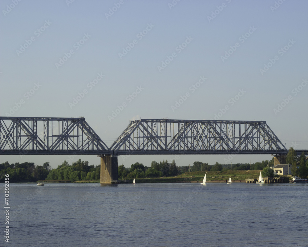 A huge beautiful railway bridge over the Volga River, a navigable span. Sailing boats sail along the river.