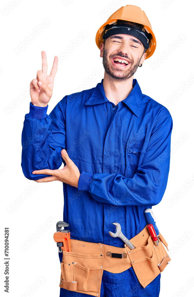 Young hispanic man wearing worker uniform smiling with happy face winking at the camera doing victory sign with fingers. number two. Young hispanic man wearing worker uniform smiling with happy face winking at the camera doing victory sign with fingers. number two.