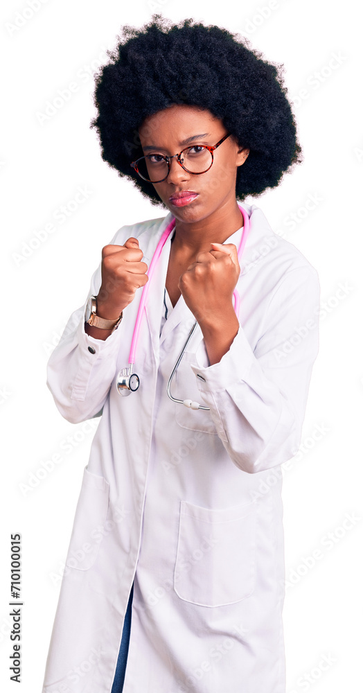 Young african american woman wearing doctor coat and stethoscope ready to fight with fist defense gesture, angry and upset face, afraid of problem