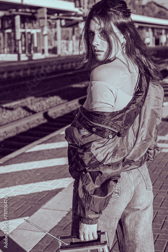 Beautiful girl dressed in 90s style with portable radio receiver in her hands posing on the platform of the train station