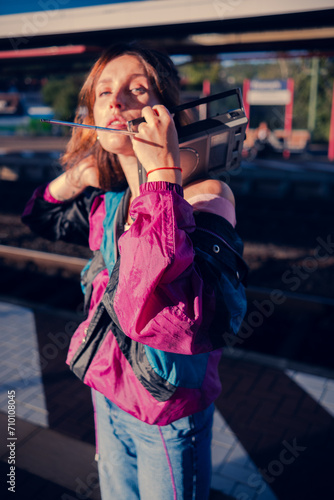 Beautiful girl dressed in 90s style with portable radio receiver in her hands posing on the platform of the train station