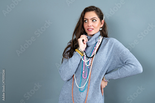 elegant woman in a long gray sweater has fun with many bead chains and jewelry, isolated on gray photo