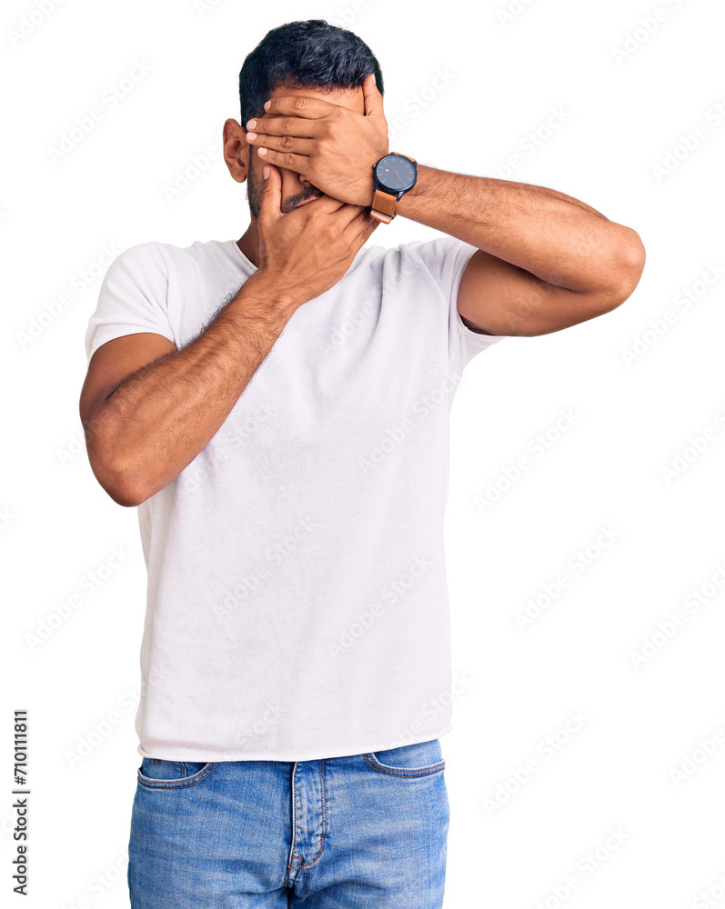 Fototapeta premium Young latin man wearing casual clothes covering eyes and mouth with hands, surprised and shocked. hiding emotion