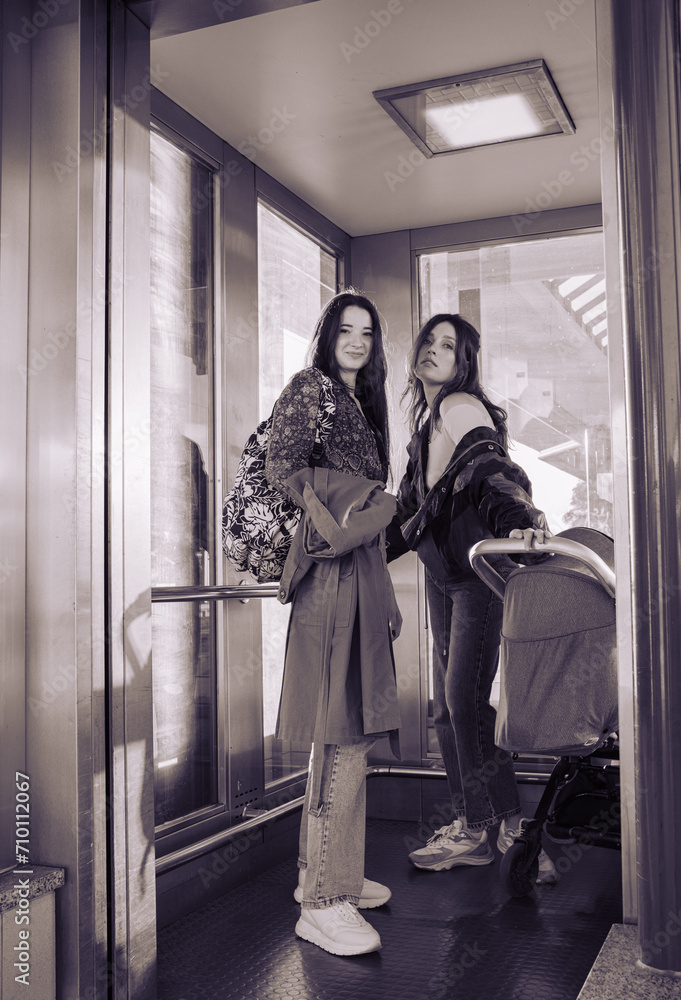 Two young girls traveling with a small child in a stroller in elevator at a train station Two young girls traveling with a small child in a stroller in elevator at a train station