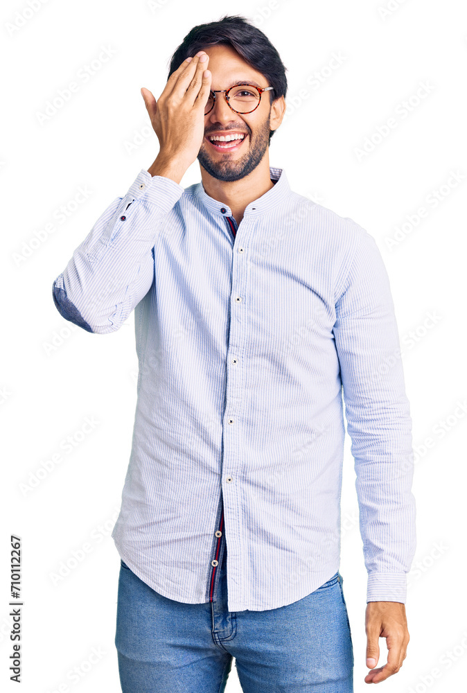 Handsome hispanic man wearing business shirt and glasses covering one eye with hand, confident smile on face and surprise emotion. Handsome hispanic man wearing business shirt and glasses covering one eye with hand, confident smile on face and surprise emotion.