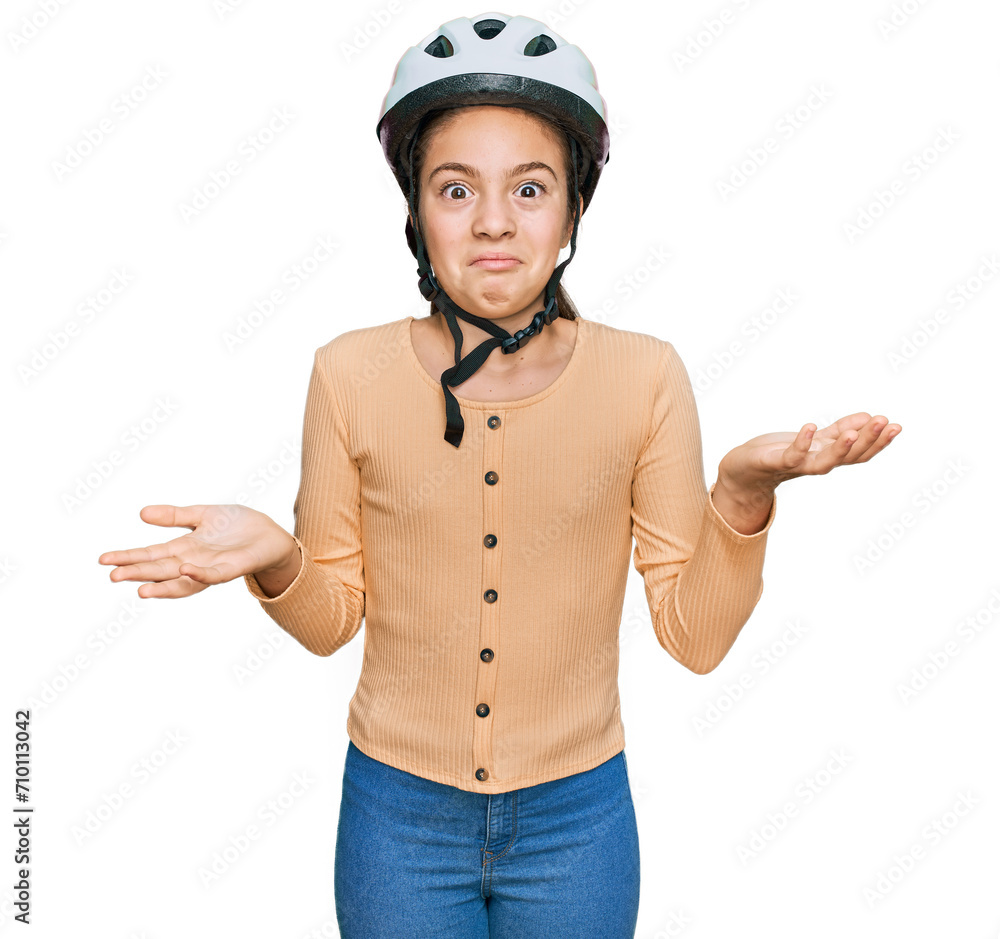 Beautiful brunette little girl wearing bike helmet clueless and confused expression with arms and hands raised. doubt concept. Beautiful brunette little girl wearing bike helmet clueless and confused expression with arms and hands raised. doubt concept.