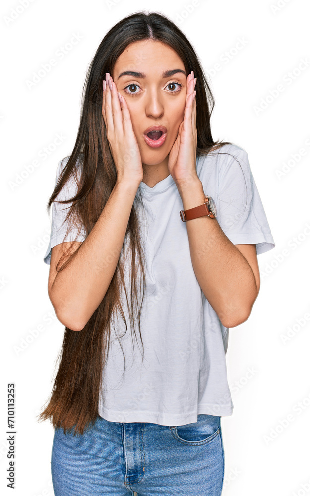 Young hispanic girl wearing casual white t shirt afraid and shocked, surprise and amazed expression with hands on face Young hispanic girl wearing casual white t shirt afraid and shocked, surprise and amazed expression with hands on face