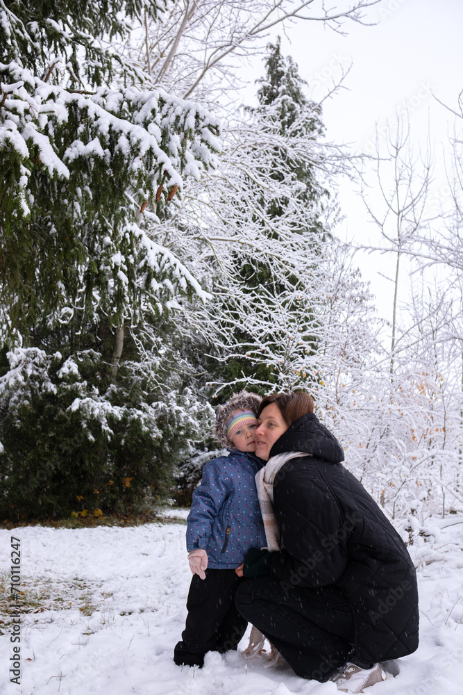 Mom with daughter in winter snowy forest. Mom kisses her daughter and warms her hands with her breath. Young girl with her daughter walking in the forest in winter. Mom with daughter in winter snowy forest. Mom kisses her daughter and warms her hands with her breath. Young girl with her daughter walking in the forest in winter.