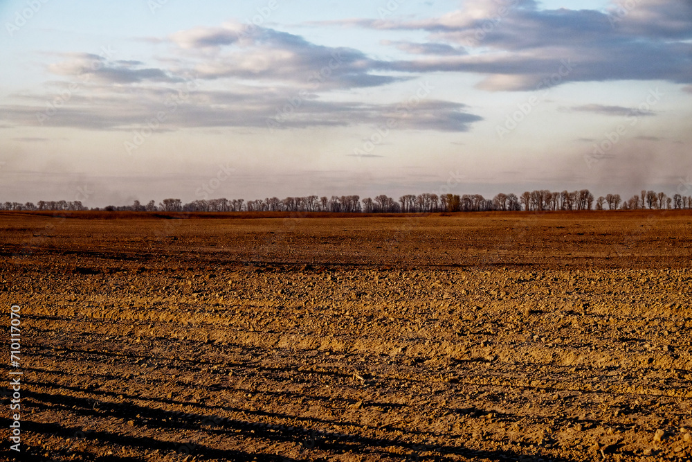 Ploughed agricultural land under a partly cloudy sky at dusk.