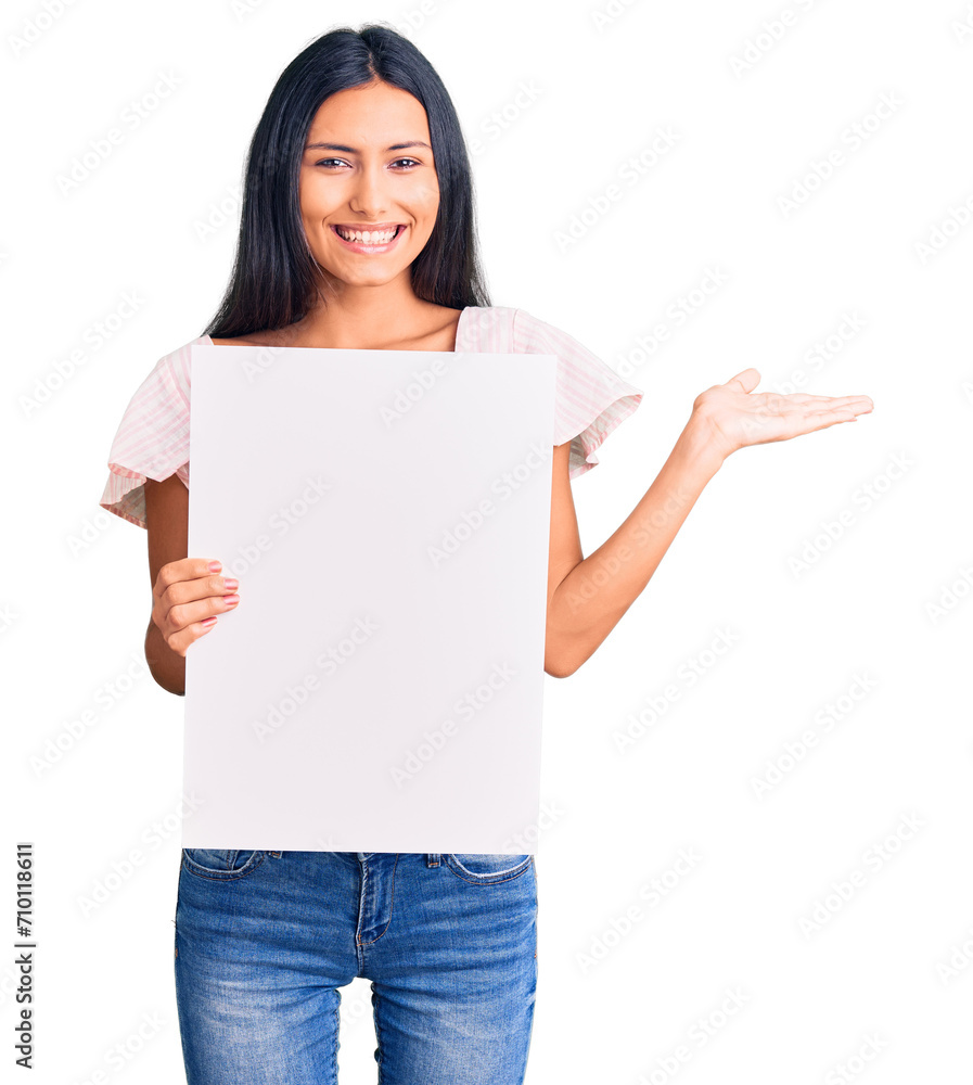 Young beautiful latin girl holding blank empty banner celebrating victory with happy smile and winner expression with raised hands Young beautiful latin girl holding blank empty banner celebrating victory with happy smile and winner expression with raised hands