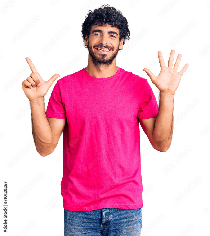 Handsome young man with curly hair and bear wearing casual pink tshirt showing and pointing up with fingers number seven while smiling confident and happy. Handsome young man with curly hair and bear wearing casual pink tshirt showing and pointing up with fingers number seven while smiling confident and happy.