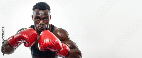 A focused athlete in a boxing stance wearing red gloves ready to strike, intensity in his eyes, against a white background. Banner with copy space.