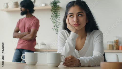 Upset Indian woman wife thinking of relationship problems after quarrel with husband on kitchen offended man stand background. Married diverse multiracial couple arguing having conflict disagreement photo