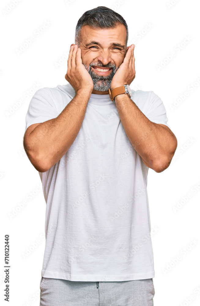 Middle age handsome man wearing casual white tshirt covering ears with fingers with annoyed expression for the noise of loud music. deaf concept. Middle age handsome man wearing casual white tshirt covering ears with fingers with annoyed expression for the noise of loud music. deaf concept.