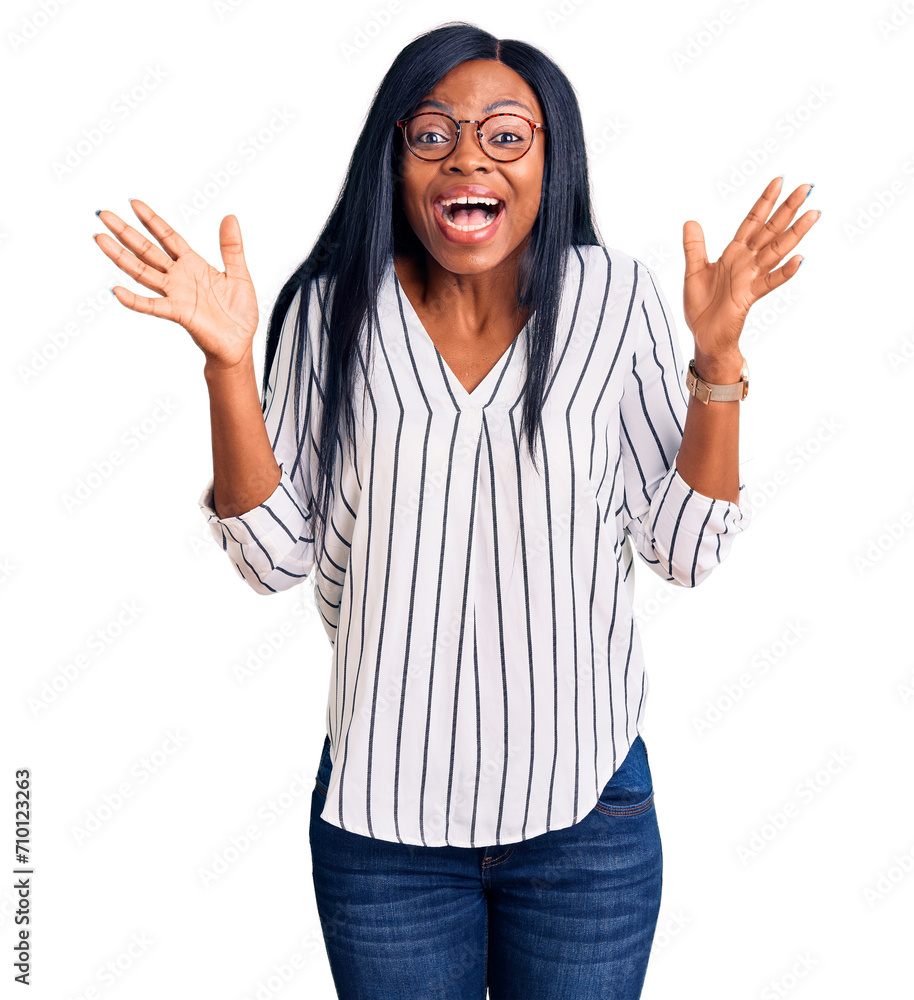 Young african american woman wearing casual clothes and glasses celebrating crazy and amazed for success with arms raised and open eyes screaming excited. winner concept Young african american woman wearing casual clothes and glasses celebrating crazy and amazed for success with arms raised and open eyes screaming excited. winner concept