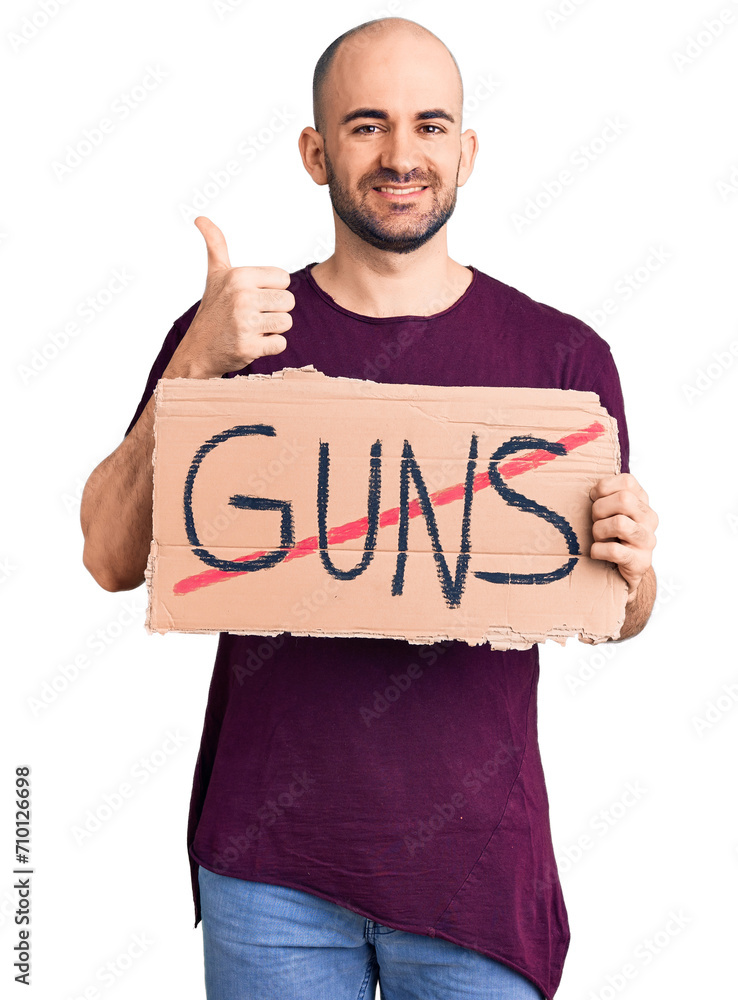 Young handsome man holding prohibited guns banner smiling happy and positive, thumb up doing excellent and approval sign Young handsome man holding prohibited guns banner smiling happy and positive, thumb up doing excellent and approval sign