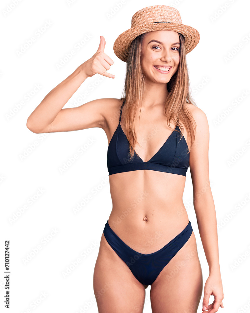 Young beautiful girl wearing bikini and hat smiling doing phone gesture with hand and fingers like talking on the telephone. communicating concepts. Young beautiful girl wearing bikini and hat smiling doing phone gesture with hand and fingers like talking on the telephone. communicating concepts.