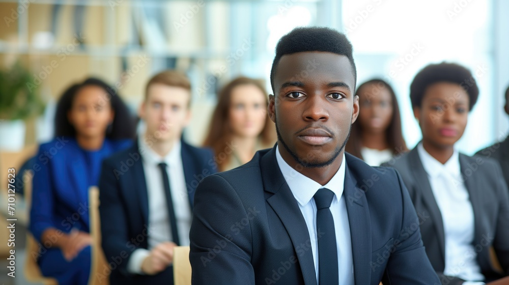 A focused young man in a sharp suit confidently awaits his interview, surrounded by potential competitors blurred in the background A focused young man in a sharp suit confidently awaits his interview, surrounded by potential competitors blurred in the background