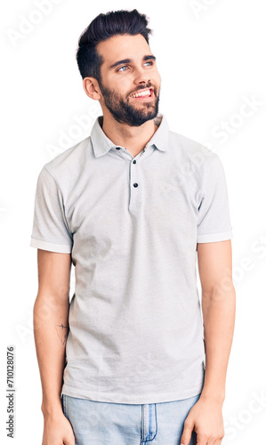 Young handsome man with beard wearing casual polo looking away to side with smile on face, natural expression. laughing confident.