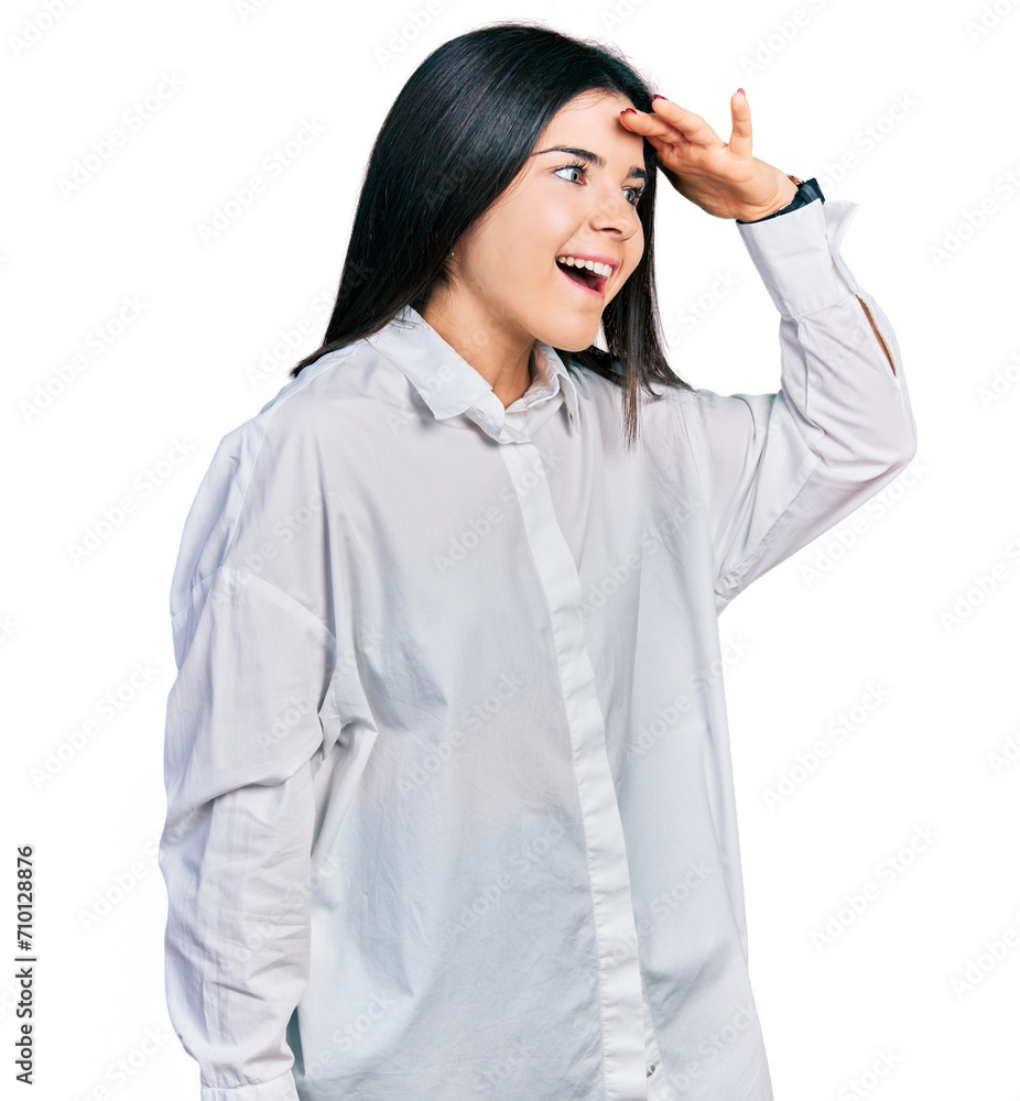 Young brunette woman with blue eyes wearing oversize white shirt very happy and smiling looking far away with hand over head. searching concept. Young brunette woman with blue eyes wearing oversize white shirt very happy and smiling looking far away with hand over head. searching concept.